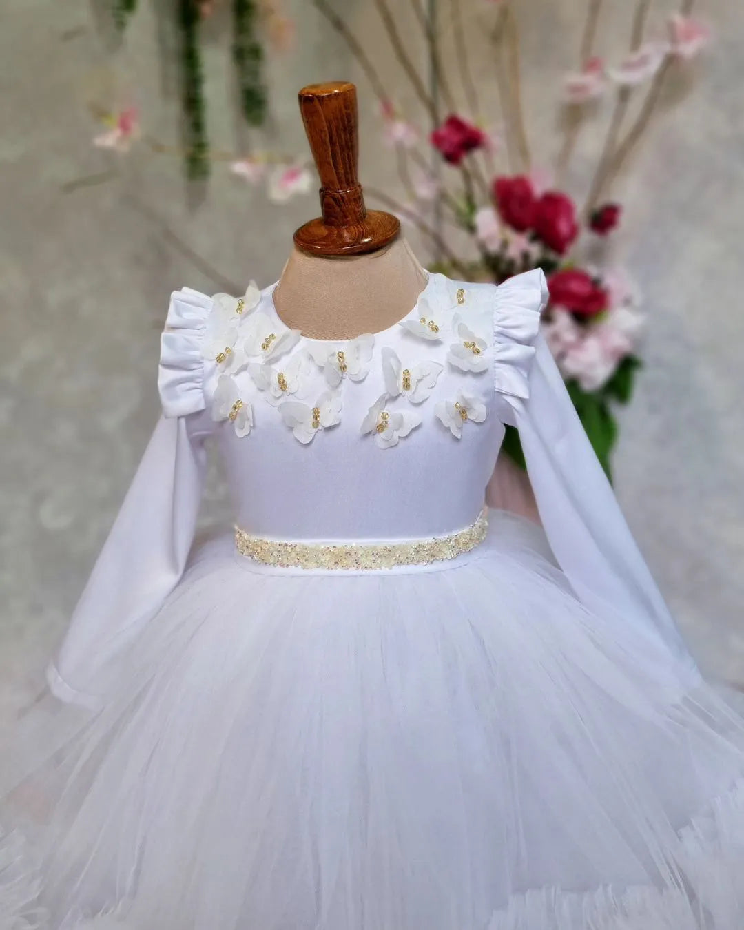 close view of white flower girl dress with butterfly accents and floral patterns.